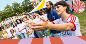 Menschen stehen gemeinsam auf einer Wiese vor einem Zirkuszelt und jubeln.