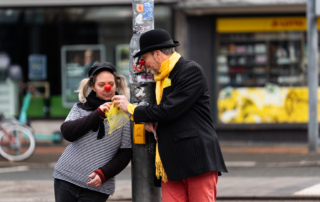 Zwei Personen sind als Clowns verkleidet und stehen an einer Straßenlaterne.