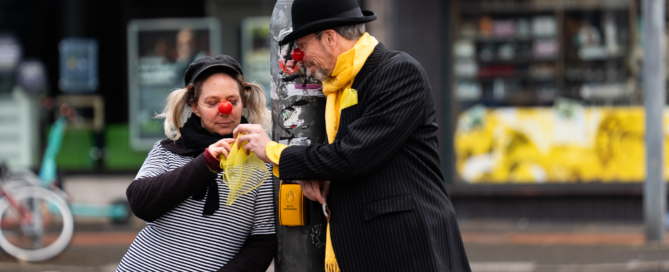 Zwei Personen sind als Clowns verkleidet und stehen an einer Straßenlaterne.