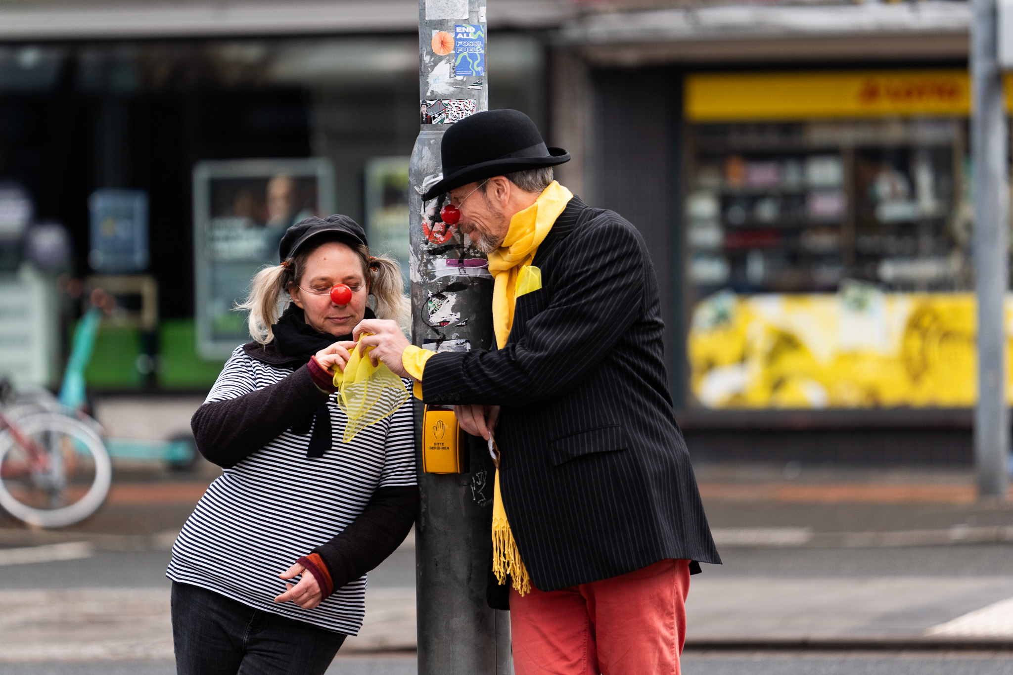 Zwei Personen sind als Clowns verkleidet und stehen an einer Straßenlaterne.