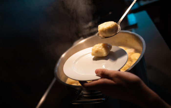 Eine Person schöpft Klöße von einem Topf auf einen Teller. Man sieht nur die Hände der Person.