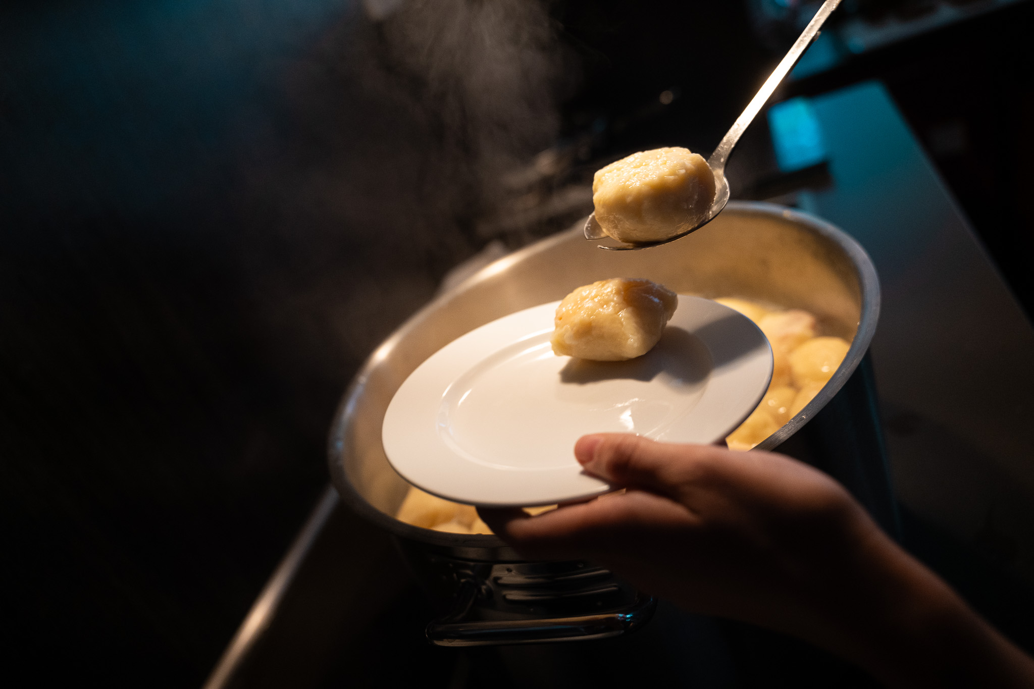 Eine Person schöpft Klöße von einem Topf auf einen Teller. Man sieht nur die Hände der Person.