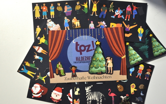 Eine Weihnachtspostkarte vom TPZ liegt auf einem Tisch. Rings herum liegen viele kleine Figuren und Tiere zum Ausschneiden.